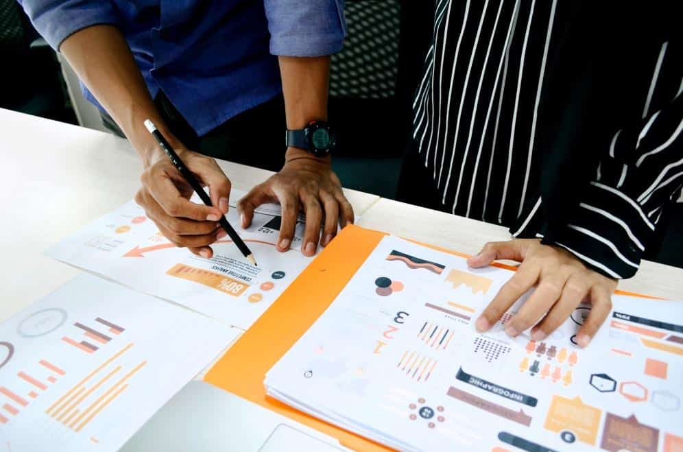 Two people reviewing marketing charts and infographic reports on a table